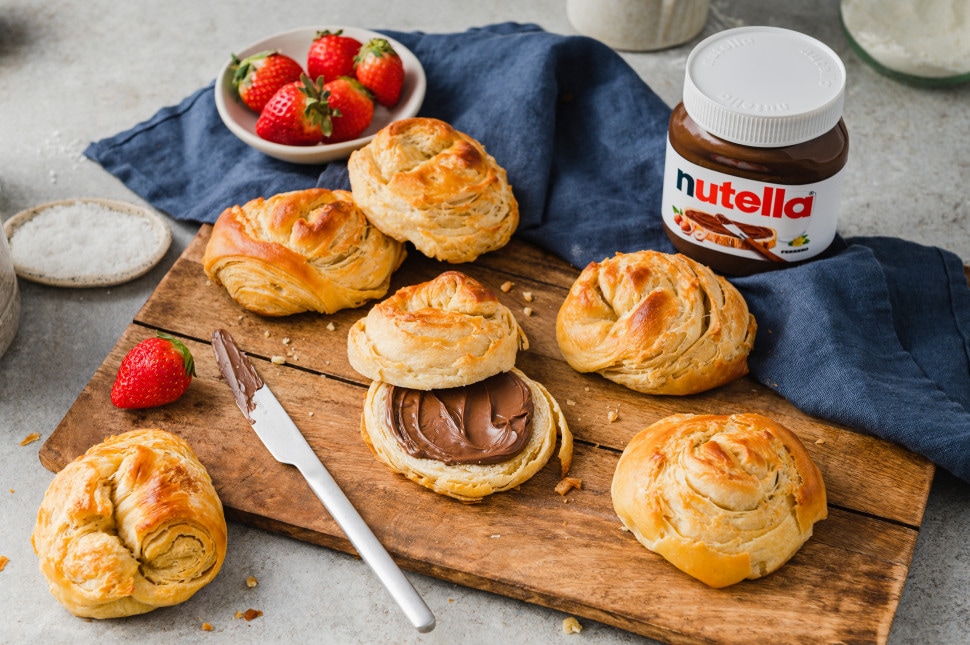 Urbanes Frühstück: Nutella-Glas neben Croissant auf Café-Tisch, stimmungsvolle Szene.