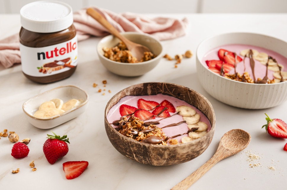 Rosarote Beeren-Smoothie-Bowls mit Erdbeeren, Bananen und Nutella-Topping auf hellem Hintergrund.