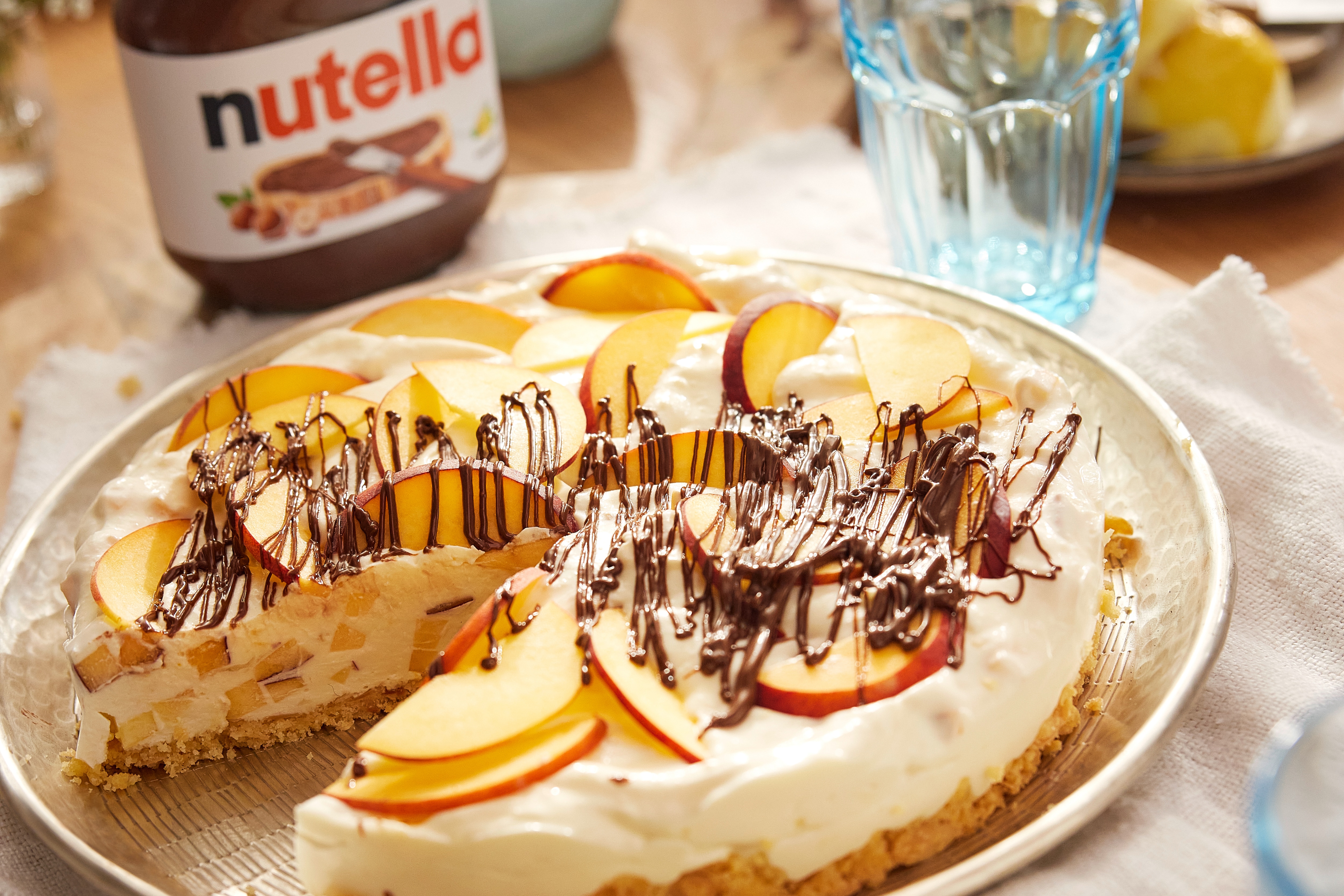 Pfirsich-Buttermilch-Torte mit Nutella-Creme und Pfirsichscheiben auf Kuchenplatte.