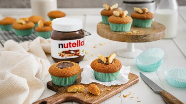 Zarte Vanille-Cupcakes mit Nutella-Frosting, Schokoladenstückchen und Nusskrokant auf Teller.