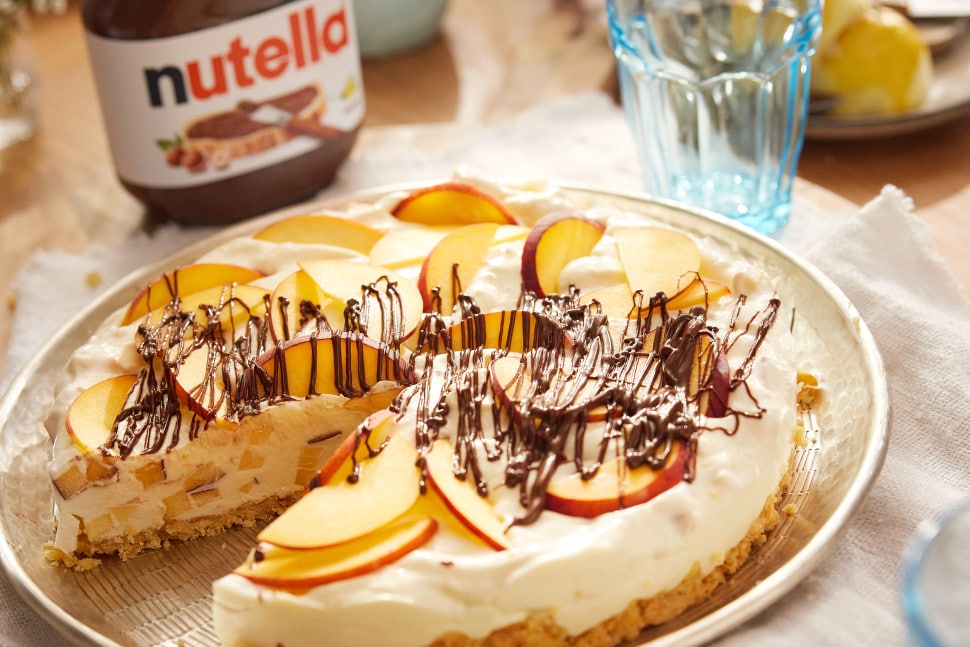 Pfirsich-Buttermilch-Torte mit Nutella-Creme und Pfirsichscheiben auf Kuchenplatte.
