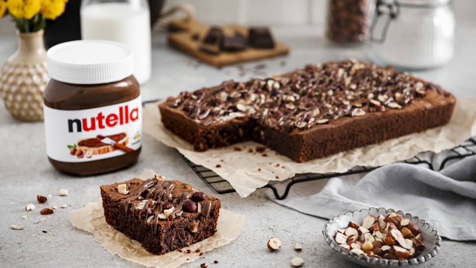 Le brownie au Nutella® est posé sur une grille de refroidissement recouverte de papier sulfurisé. Un carré a été découpé dans le brownie et posé à côté d'un pot de Nutella®.