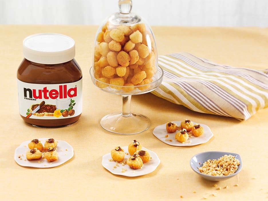 Small struffoli balls drizzled with Nutella and decorated with colorful sprinkles.