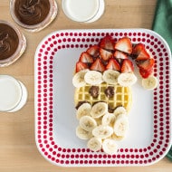 Santa-shaped waffle decorated with Nutella and festive holiday toppings.