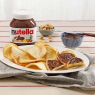 Thin almond tegole cookies layered with Nutella, stacked on parchment.