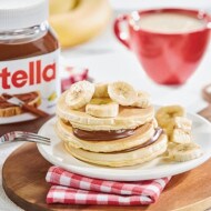 Nutella spread on toast beside fresh strawberries and a small jar.