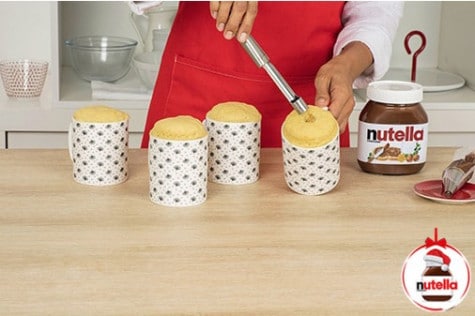 A baker is digging a hole in a centre of baked mug cakes using a apple corer.