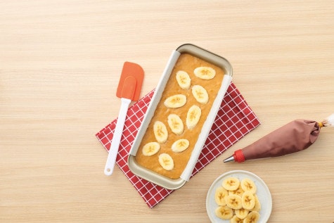 Top view of banana bread dough in cake pan with banana slices neatly arranged on top.