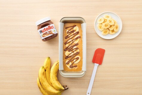 Overhead view of banana bread dough in the cake pan, with banana slices neatly arranged on top and Nutella® poured on top in a zigzag pattern.