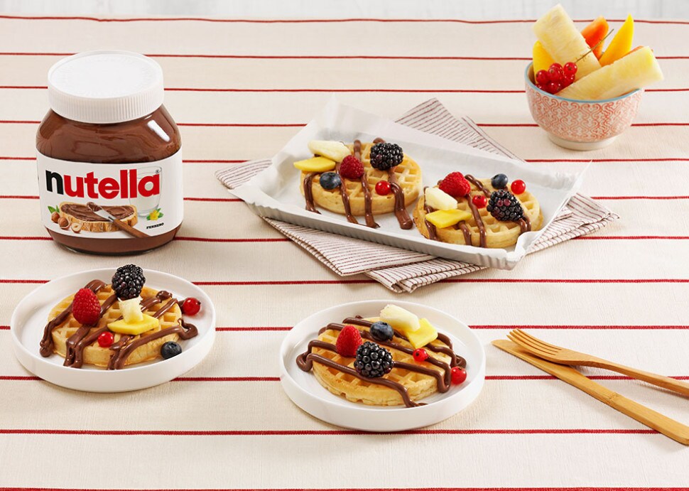 Waffles topped with Nutella and assorted fresh fruits on a white plate.