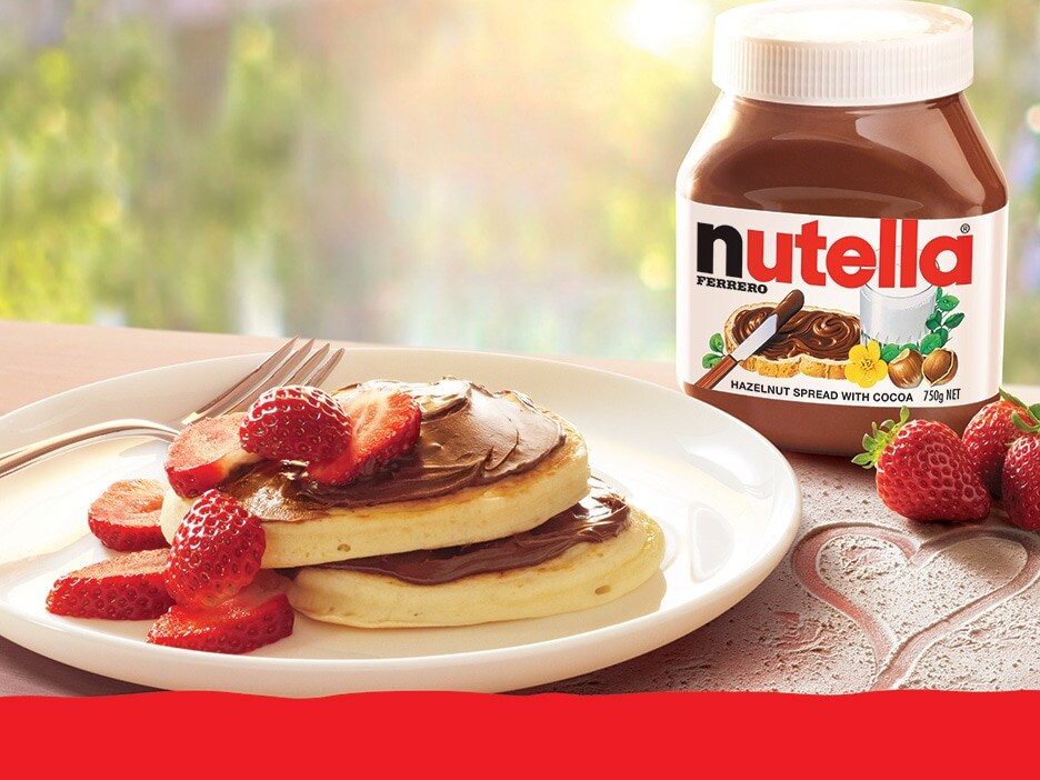 Pancake stack layered with Nutella, fresh strawberries, and syrup drizzle.