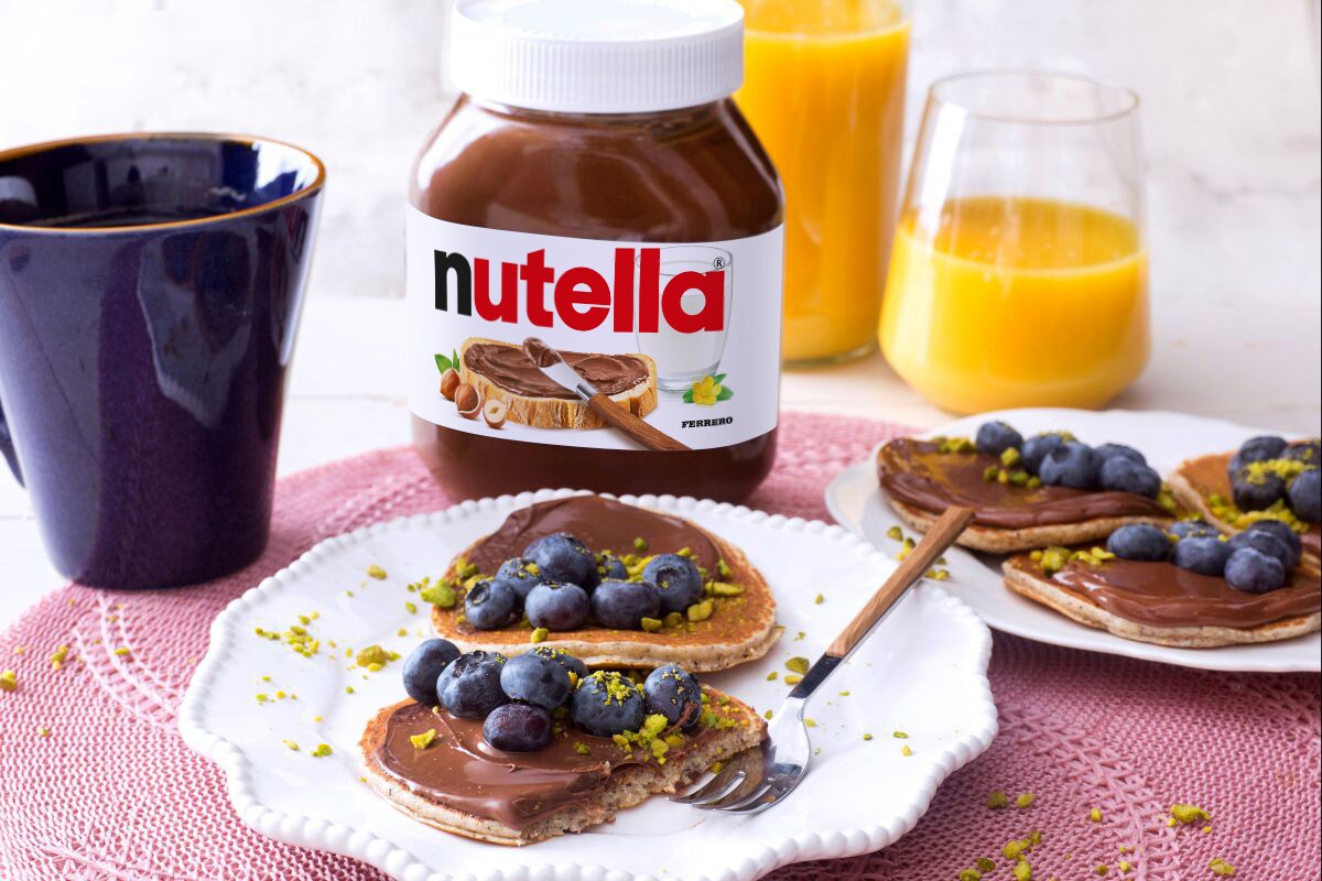 Pancake impilati con sciroppo e Nutella su piatto rustico.