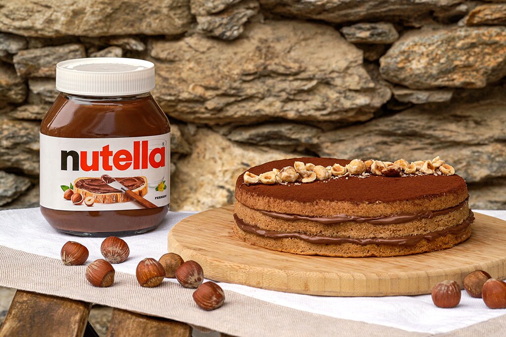Torta alle nocciole farcita e ricoperta di Nutella su tavola.