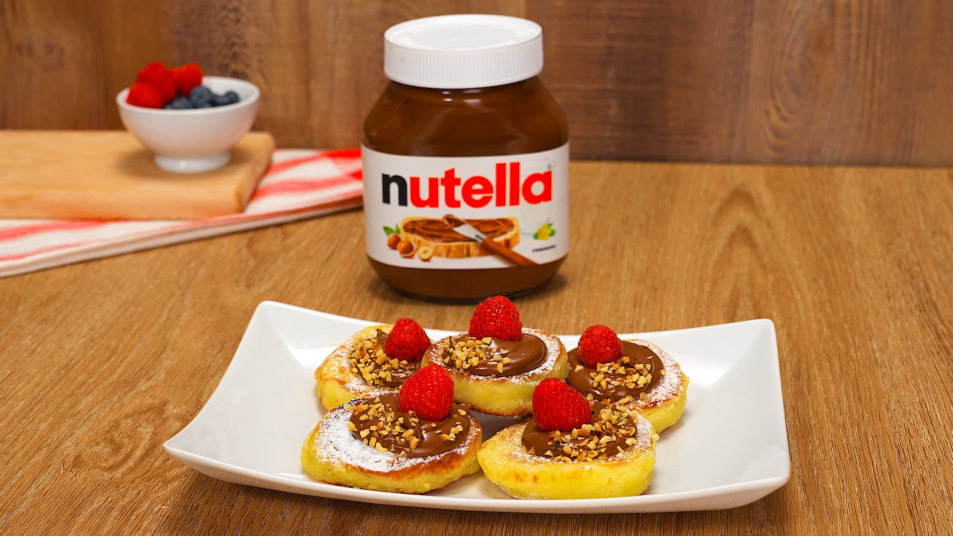 Syrniki fritti serviti con Nutella e frutta fresca accanto.