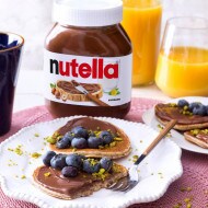 Pancake impilati con sciroppo e Nutella su piatto rustico.