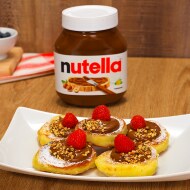Syrniki fritti serviti con Nutella e frutta fresca accanto.
