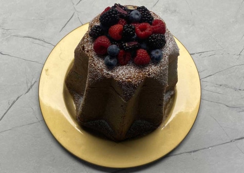 Il Pandoro è adagiata su un piatto d'oro, con una spolverata di zucchero a velo e bacche decorate sulla superficie.