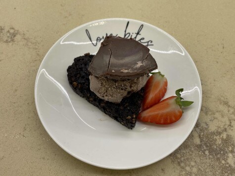 Una pallina di Nutella Gelato si trova sopra un cuore di crumble. Due fette di fragola sono posizionate accanto al dolcetto a forma cuore.