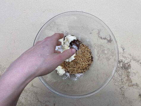 Vista dall'alto di una grande ciotola di vetro contenente gli ingredienti per fare il crumble al cioccolato. Una mano sta mescolando insieme gli ingredienti.