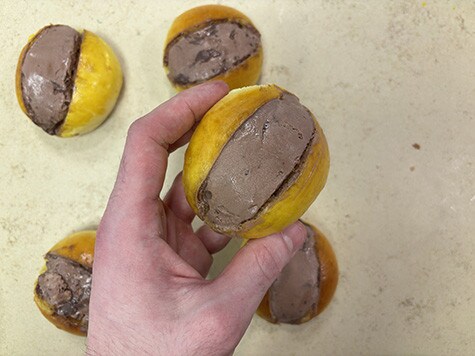 Vista dall'alto di una mano che regge un maritozzo di Carnevale, ripieno di Nutella Gelato. Sullo sfondo, altri quattro maritozzi di Carnevale.