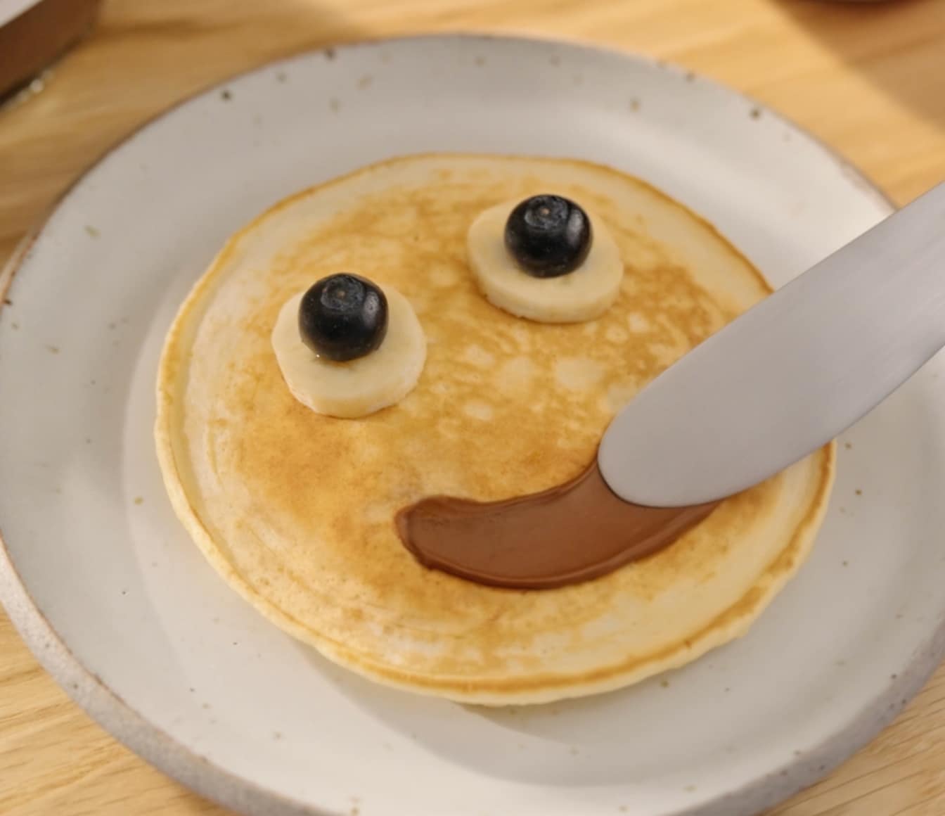 Stack of pancakes topped with Nutella smiley face on plate.