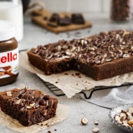 Chocolate brownies topped with Nutella and served on a rustic board.