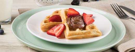 Belgian waffle topped with Nutella and fresh berries on a plate.