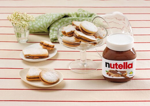 Round sandwich biscuits generously filled with Nutella, stacked on plate.