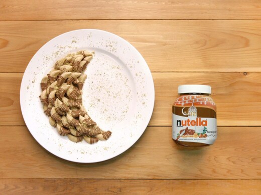 بسكويت مرتب على شكل هلال على طبق أبيض؛ بجانبهم جرة نوتيلا على طاولة خشبية، محاطة بالفتات المرشوش.