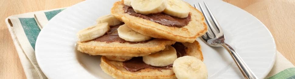 Stack of banana Nutella pancakes drizzled with syrup and sliced bananas.
