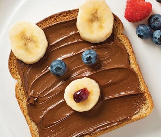 Teddy-bear-shaped toast spread with Nutella and decorated with fresh fruit.