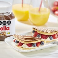 Panqueques con Nutella, crema batida y frutas variadas, presentación apetecible.