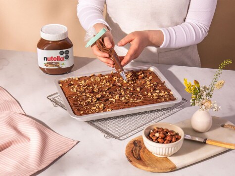 Un repostero decora el brownie horneado, que luego se unta en una bandeja de horno con avellanas y Nutella®.