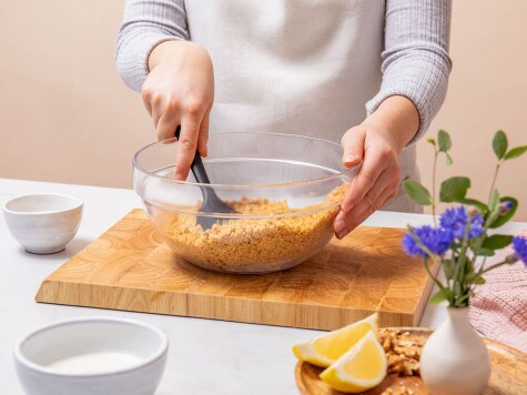 Un repostero mezcla nueces picadas, galletas trituradas y mantequilla en un recipiente de vidrio con una espátula de silicona.