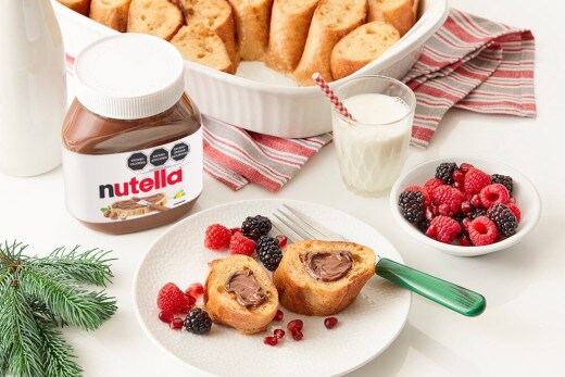 Pan francés horneado, dorado, rebanadas servidas con Nutella y fruta fresca.