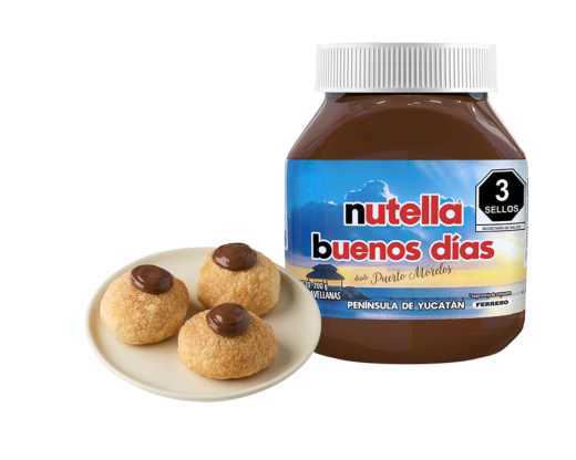 Un frasco de Nutella Buenos Días está junto a un plato con tres galletas cubiertas con Nutella. La etiqueta muestra una escena del amanecer con el texto "Desde Puerto Morelos y Yucatán