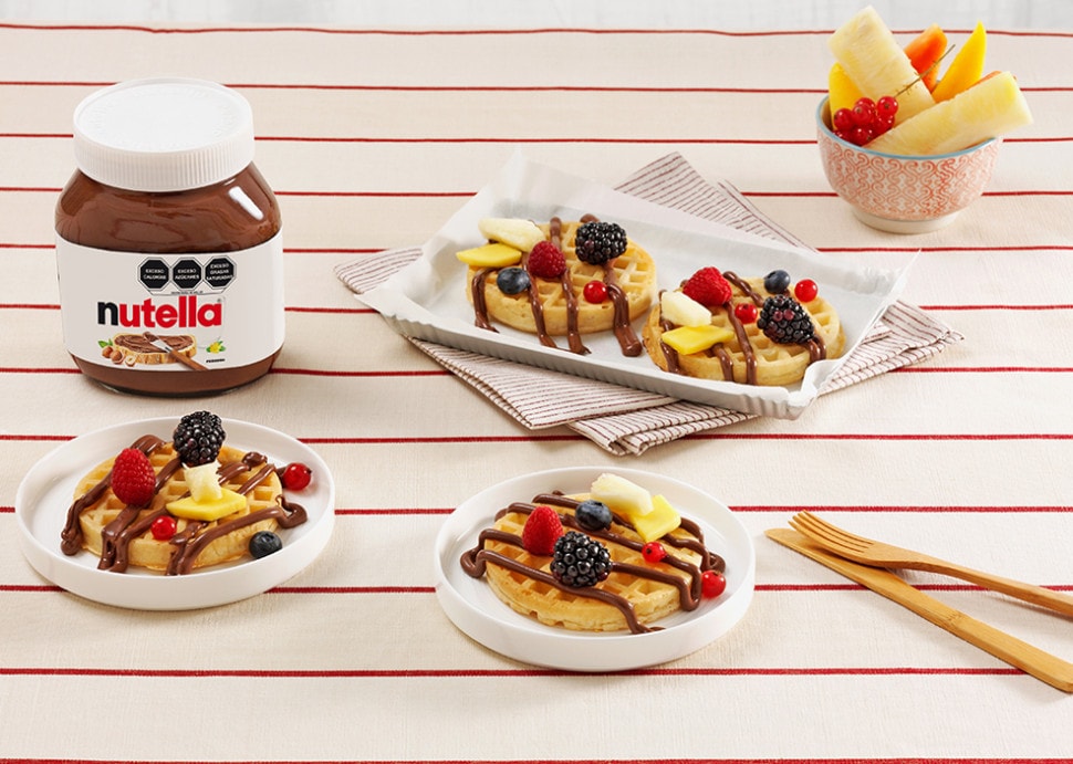 Waffles crujientes con Nutella y frutas frescas, servidos con sirope.