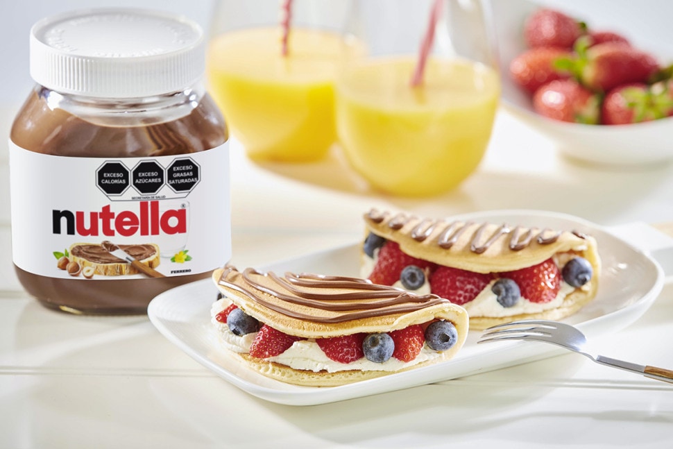 Panqueques con Nutella, crema batida y frutas variadas, presentación apetecible.