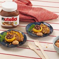 Brzoskwinie z ciasteczkami Amaretti i kremem Nutella® podane na granatowych talerzykach