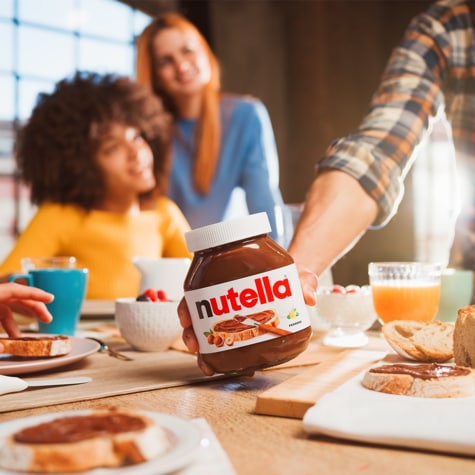 Nutella jar next to toast, fruit, and coffee in breakfast scene.