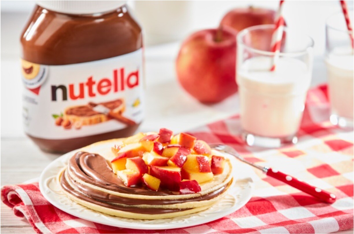 Pancakes topped with apple slices, Nutella spread and maple syrup.