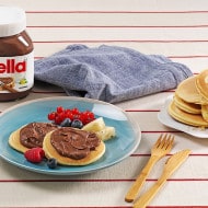 Mini pancakes stacked with Nutella and assorted fresh fruit on plate.