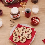 Christmas note cookies decorated with Nutella and festive icing on tray.