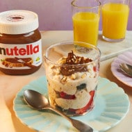 A jar of overnight oats with mixed berries, almonds, and Nutella®, served with a glass of juice and Nutella® jar.