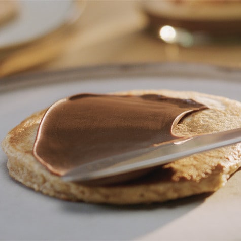 Stack of pancakes with Nutella between layers and sliced strawberries.