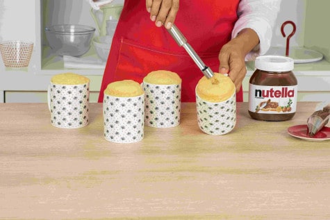 A baker is digging a hole in a centre of baked mug cakes using a apple corer.
