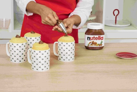 A baker is using a piping bag to fill each cake with a 15g portion of Nutella®.