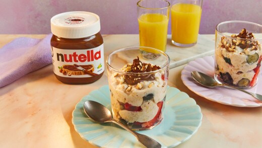 A jar of overnight oats with mixed berries, almonds, and Nutella®, served with a glass of juice and Nutella® jar.