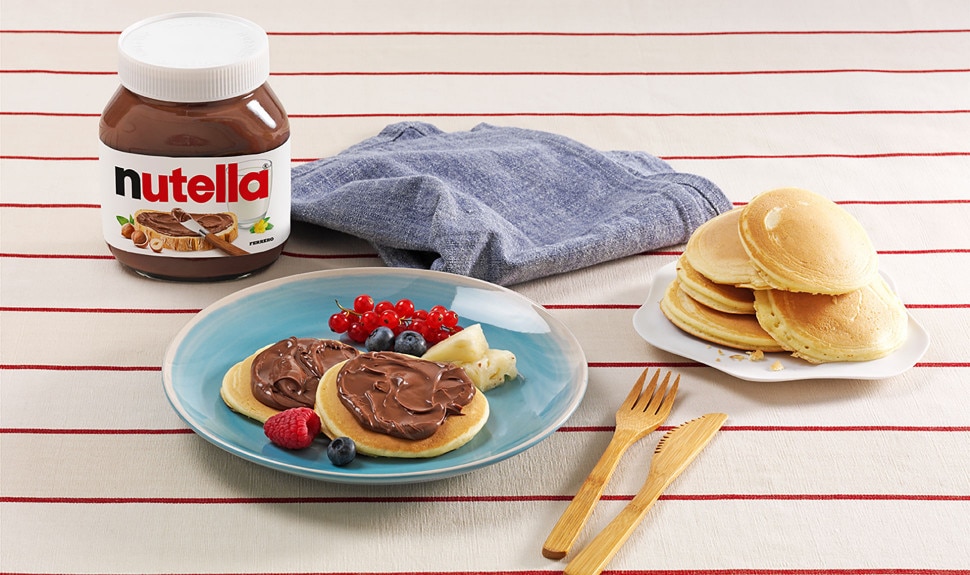 Mini pancakes stacked with Nutella and assorted fresh fruit on plate.