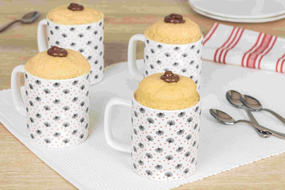 Individual mug cake topped with Nutella and chocolate shavings, served warm.